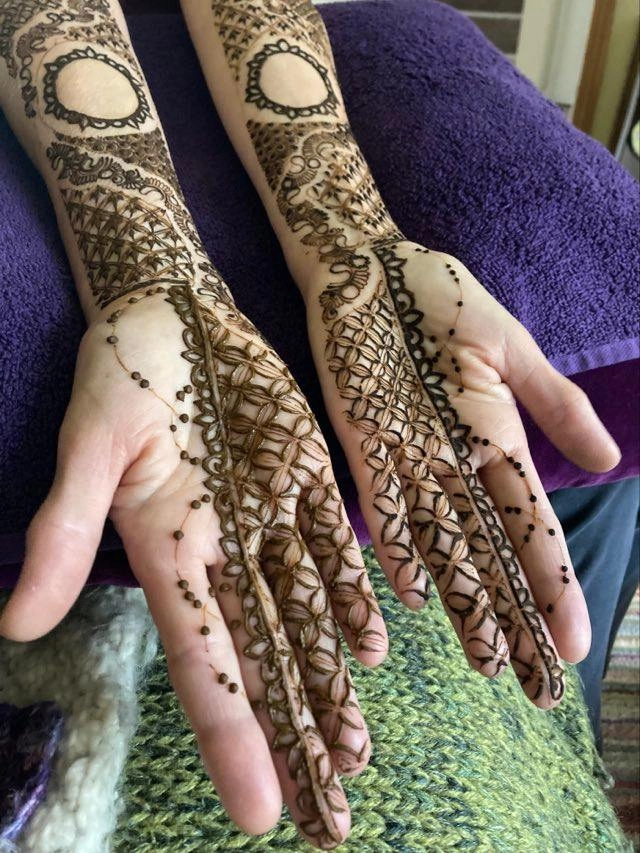 Underside of two hands with bridal henna going up the forearm